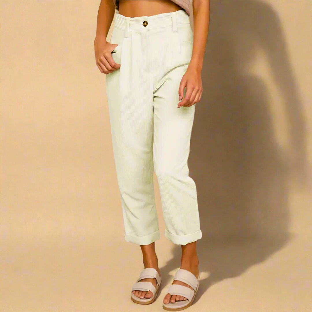 Pantaloni bianchi a vita alta, stile casual, con risvolto. Indossati con sandali beige su sfondo neutro. Moda donna, abbigliamento estivo.