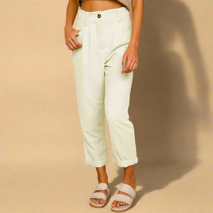 Pantaloni bianchi a vita alta, stile casual, con risvolto. Indossati con sandali beige su sfondo neutro. Moda donna, abbigliamento estivo.