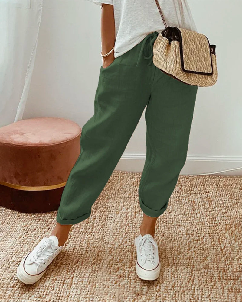 Donna con pantaloni verdi casual, borsa a tracolla beige e sneakers bianche. Moda estiva, abbigliamento comodo, stile urbano.