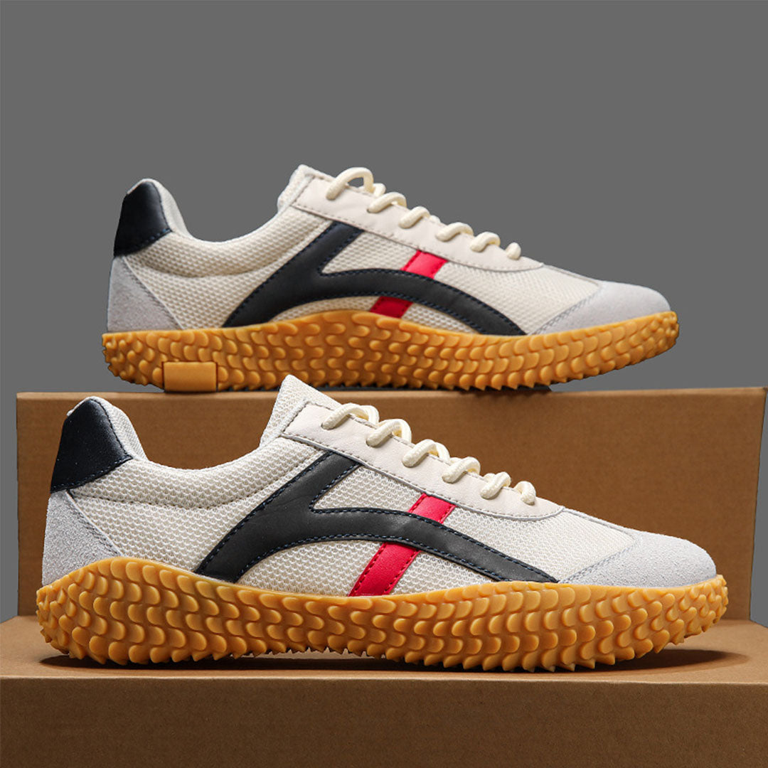 Scarpe da ginnastica bianche con suola in gomma gialla, dettagli neri e rossi, su sfondo grigio. Design moderno e sportivo, calzature casual.