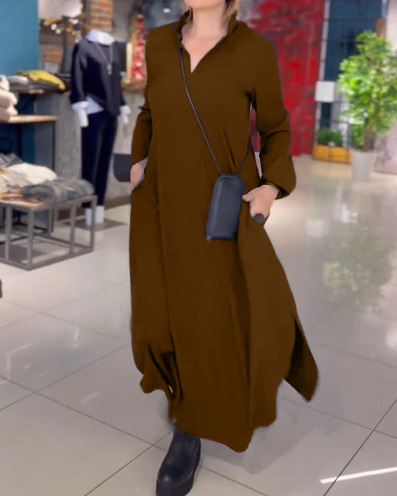 Donna in abito lungo marrone con borsa a tracolla nera, in negozio di moda. Scarpe nere, ambiente moderno con piante e abbigliamento esposto.