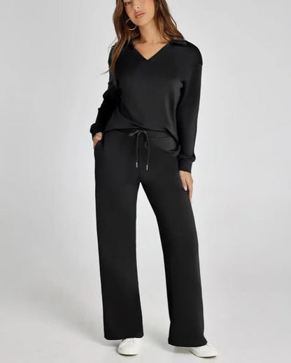 Donna in tuta nera elegante, con cappuccio e pantaloni larghi, indossa scarpe bianche. Moda casual chic, abbigliamento comodo per il tempo libero.