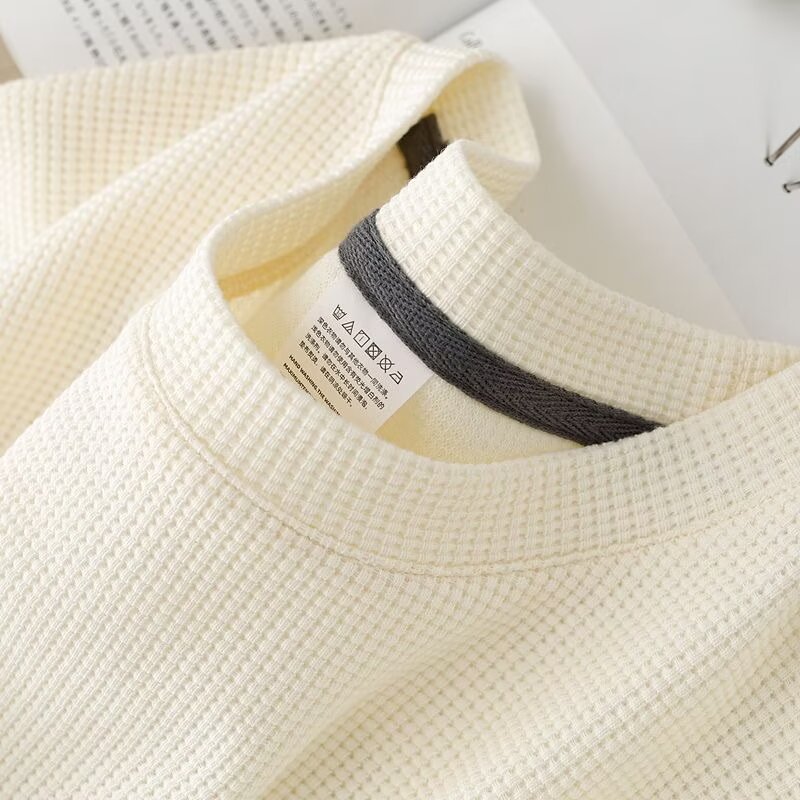 Maglia termica bianca in tessuto waffle, etichetta visibile, dettaglio del colletto grigio. Abbigliamento invernale caldo e confortevole.