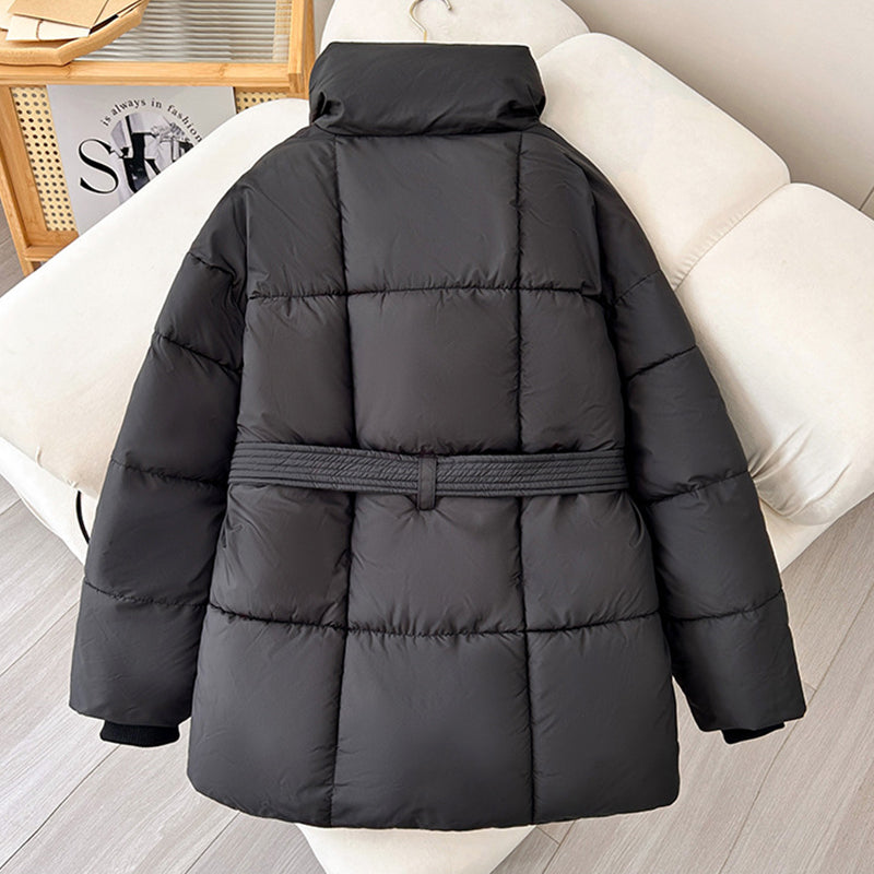 Giacca invernale nera imbottita con cintura, design trapuntato, collo alto, su divano chiaro. Moda donna, abbigliamento caldo, stile casual.