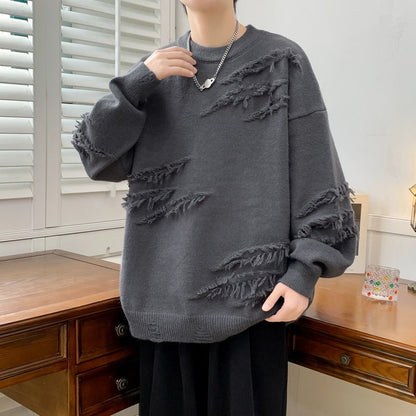 Maglione grigio oversize con dettagli strappati, indossato da una persona in una stanza con mobili in legno e finestre con persiane bianche.