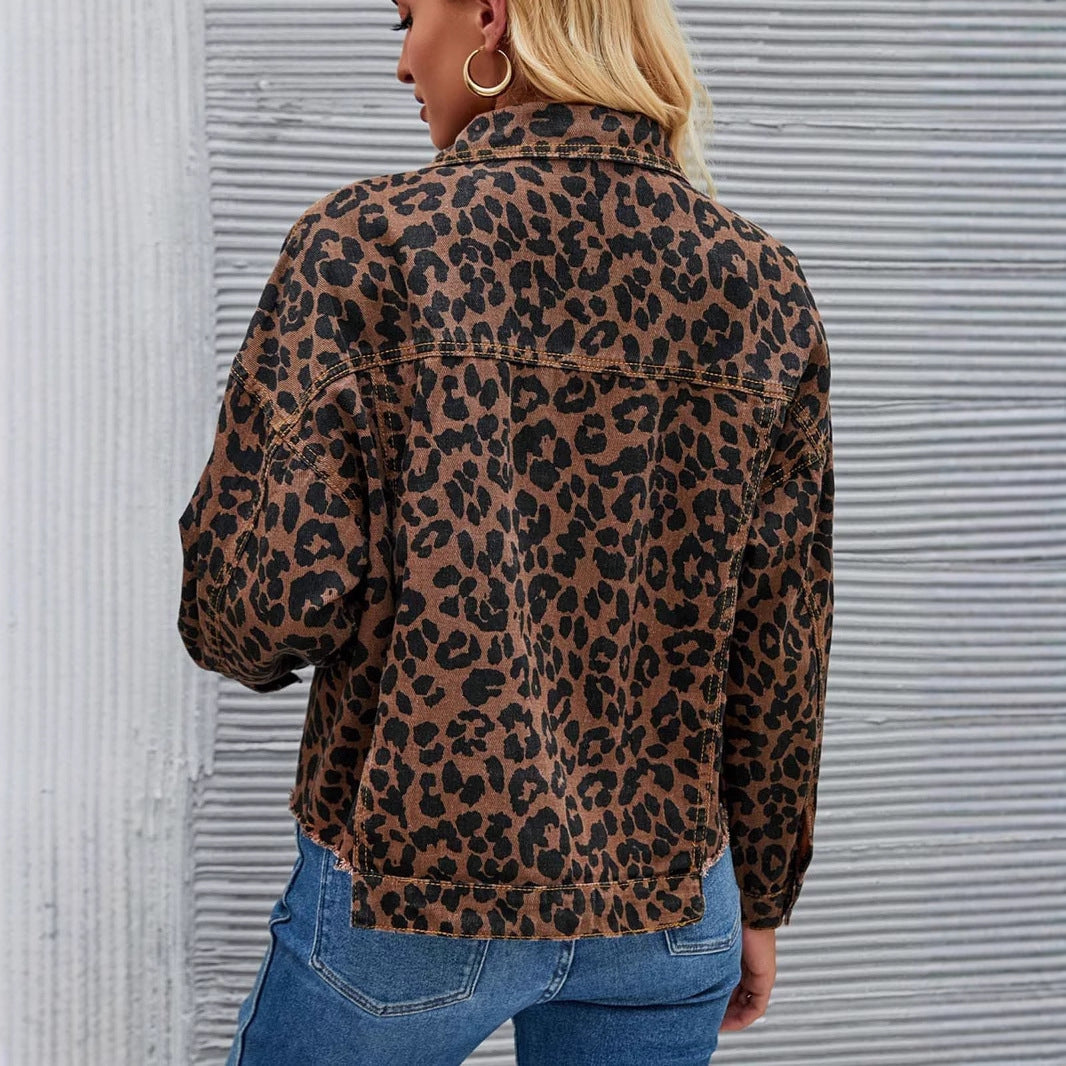 Giacca donna stampa leopardata, moda autunno, tessuto casual, abbinata a jeans blu, sfondo a righe grigie, stile urbano chic.