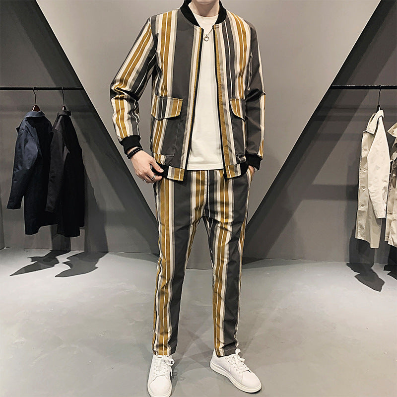 Completo uomo a righe verticali marroni e gialle, giacca e pantaloni abbinati, indossato con sneakers bianche, moda casual elegante.