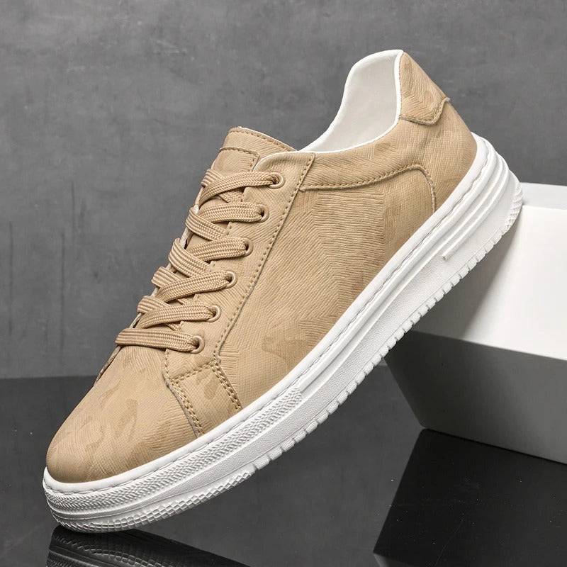 Scarpa da ginnastica beige su sfondo grigio, design moderno con suola bianca. Calzatura casual unisex, perfetta per moda urbana e comfort quotidiano.