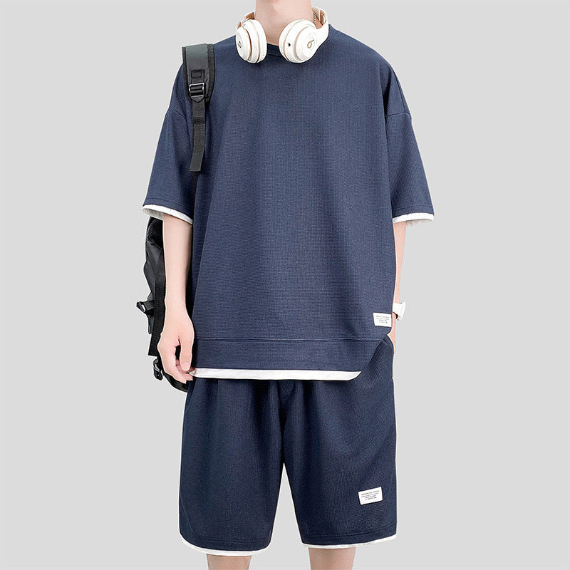 Giovane con cuffie indossa t-shirt e pantaloncini blu, zaino nero. Moda casual uomo, abbigliamento estivo, streetwear moderno.