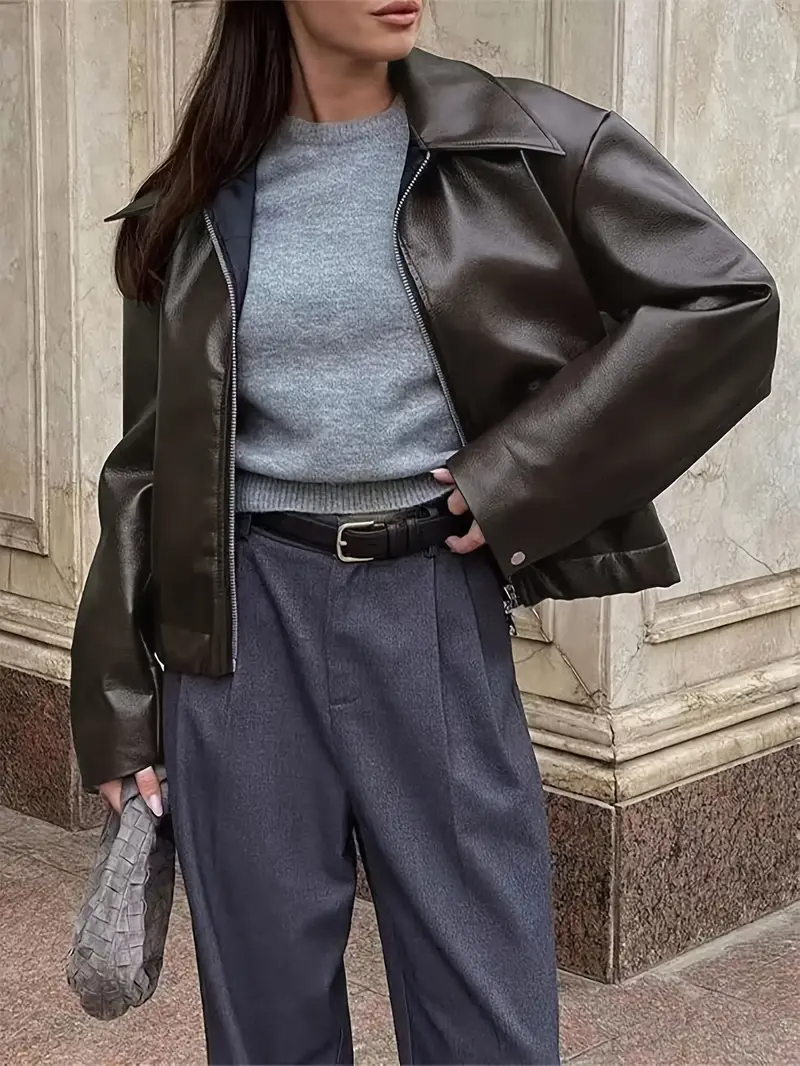 Giacca in pelle nera, maglione grigio, pantaloni blu, borsa intrecciata. Moda autunnale donna, stile urbano elegante.