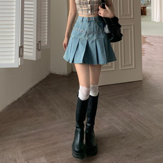 Donna con top a quadri e gonna di jeans con catena di cuori, stivali neri alti e calze bianche in una stanza moderna. Moda casual femminile.