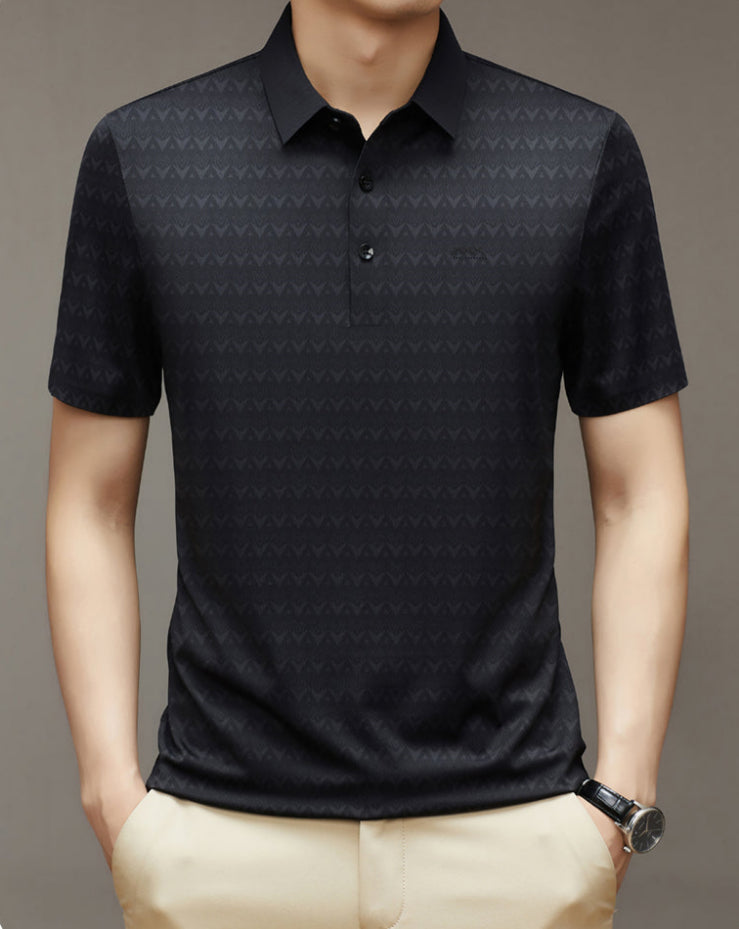 Uomo con polo nera a maniche corte, motivo geometrico, colletto classico, abbinata a pantaloni beige. Stile casual elegante.
