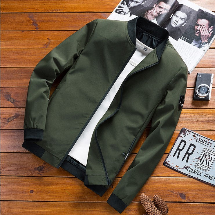 Giacca bomber verde militare su tavolo in legno, con fotocamera vintage e targa decorativa. Moda uomo casual, stile autunnale.