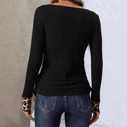 Maglia nera a coste con maniche lunghe e polsini leopardati, indossata da una donna di spalle, abbinata a jeans blu. Moda casual autunnale.