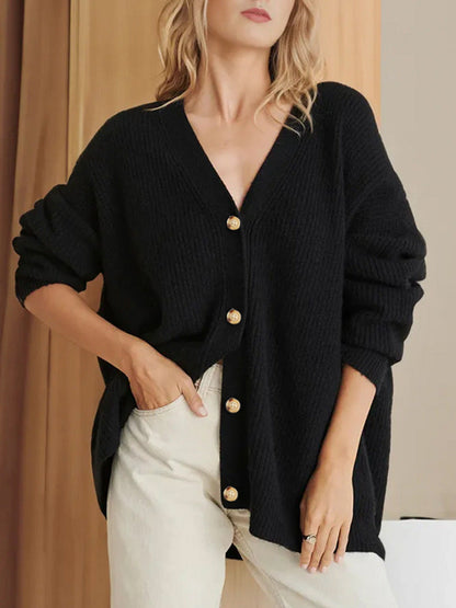 Donna indossa cardigan nero oversize con bottoni dorati, abbinato a pantaloni chiari. Moda autunnale elegante e casual.