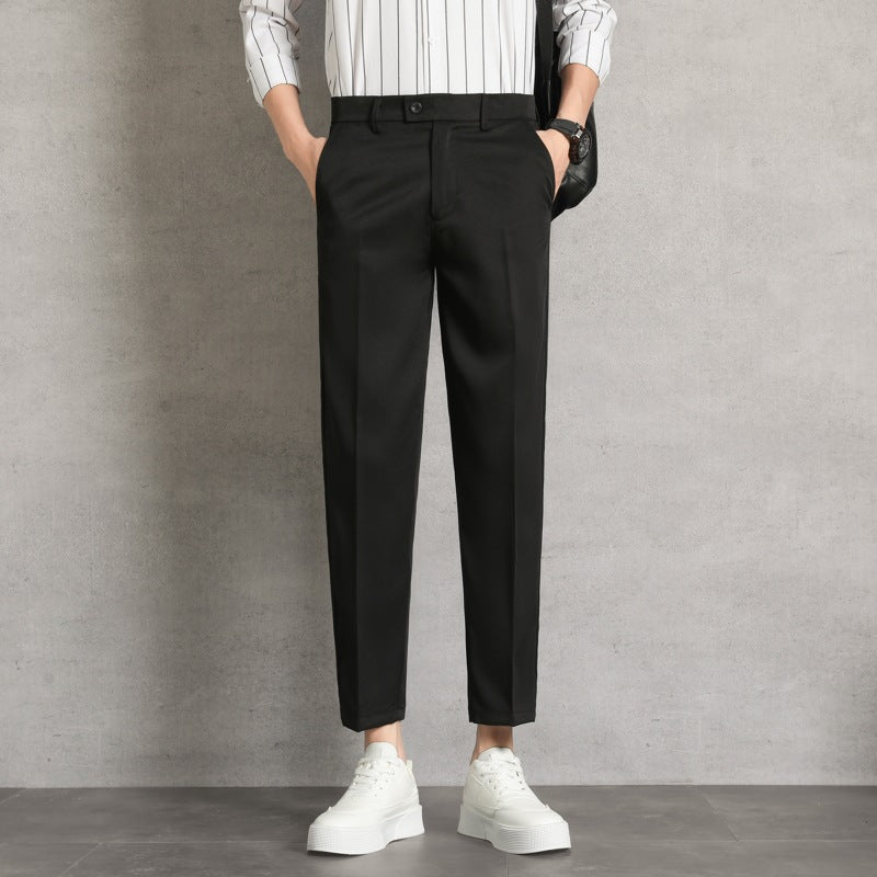 Pantaloni neri eleganti da uomo, abbinati a camicia a righe bianche e scarpe da ginnastica bianche, su sfondo grigio minimalista.