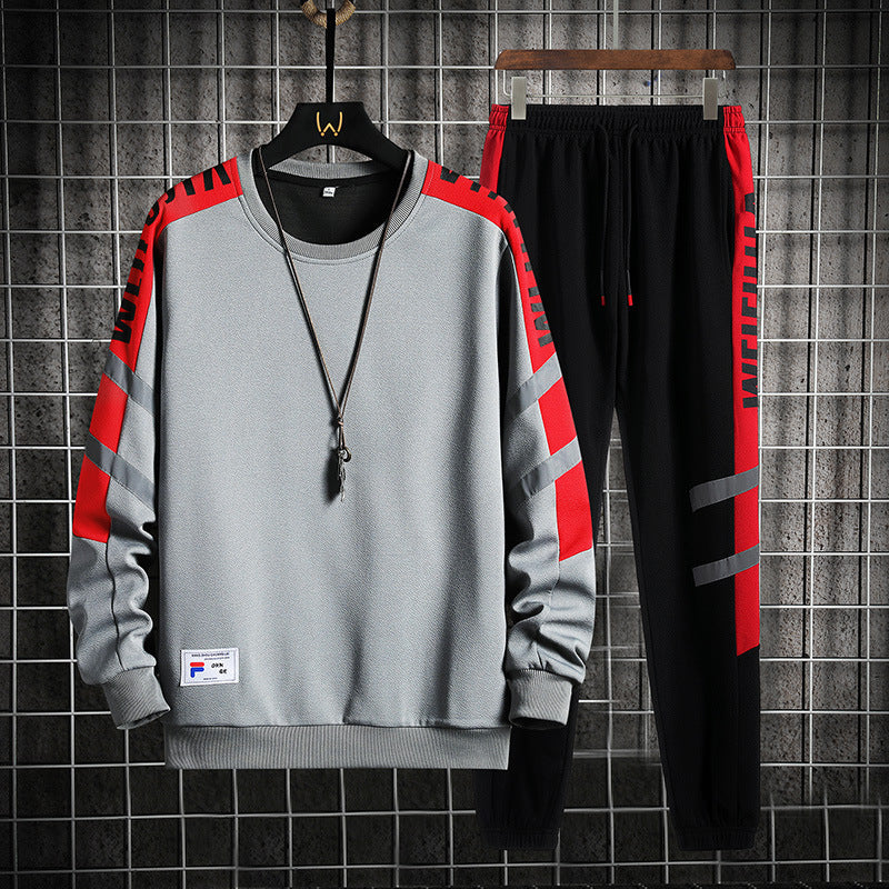 Tuta sportiva uomo grigia e nera con dettagli rossi, felpa e pantaloni, stile casual, appesa su griglia metallica, moda streetwear.