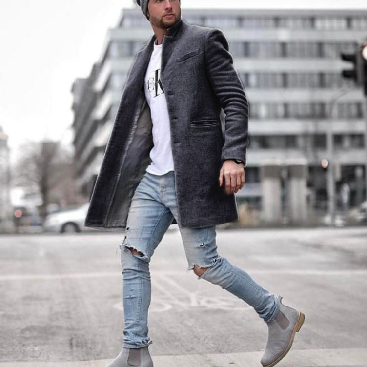 Uomo alla moda con cappotto grigio scuro, jeans strappati e stivali grigi, cammina in città. Stile urbano, abbigliamento invernale casual.