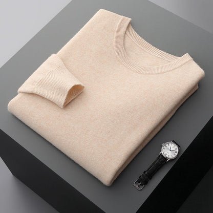 Maglione beige in cashmere piegato su tavolo grigio, accanto a orologio da polso elegante con cinturino in pelle nera e quadrante bianco.