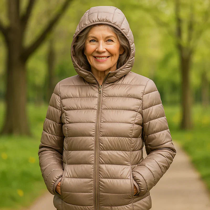 Donna sorridente con giacca imbottita beige, cappuccio alzato, in un parco verde. Moda autunnale, abbigliamento caldo, passeggiata all'aperto.