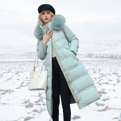 Donna con cappotto lungo verde menta invernale, berretto nero e borsa bianca, in paesaggio innevato. Moda invernale, abbigliamento caldo.