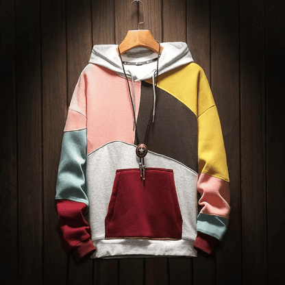 Felpa con cappuccio multicolore a blocchi, design geometrico, tasca frontale, appesa su sfondo in legno scuro. Moda casual, abbigliamento autunnale.