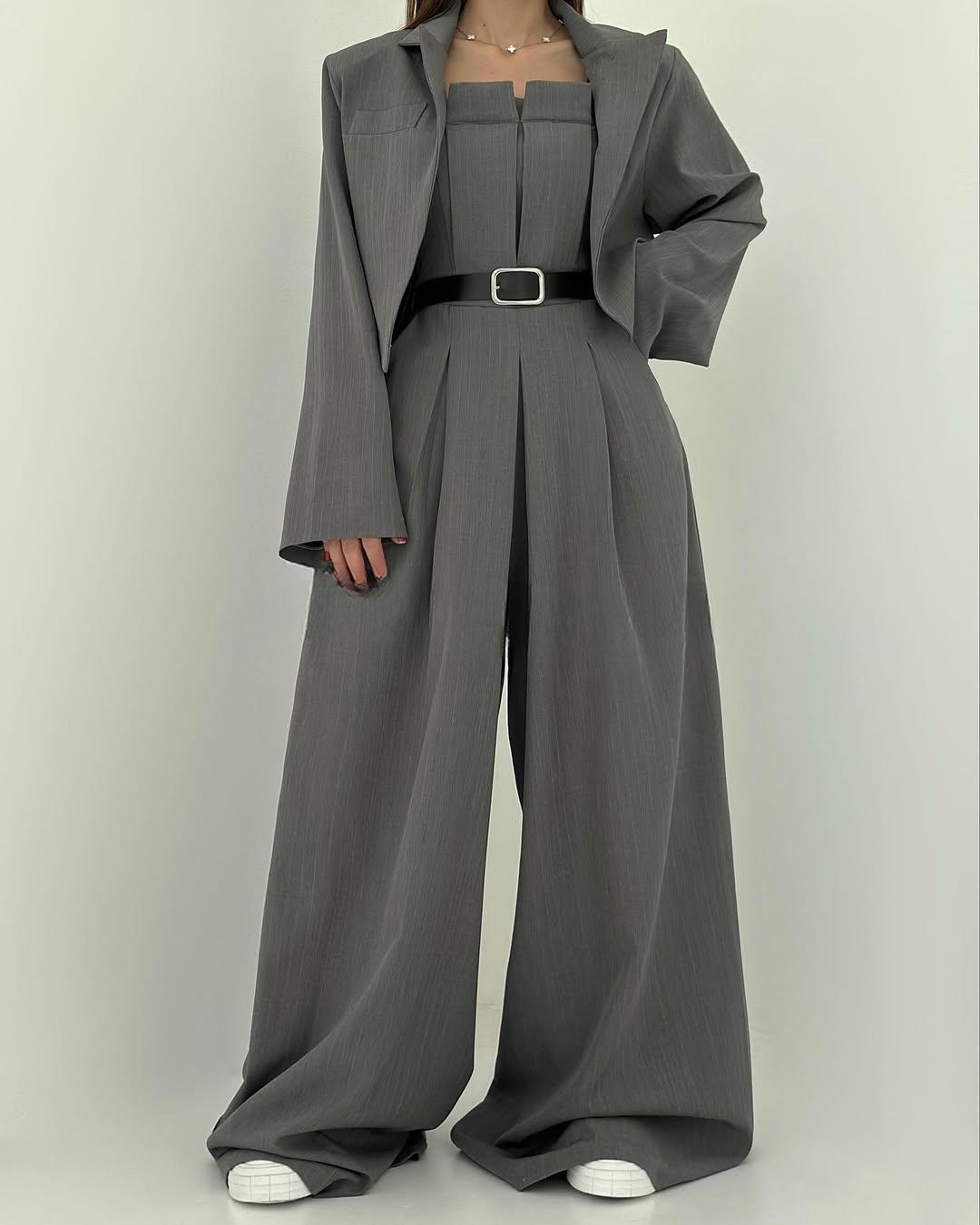 Completo elegante grigio con giacca oversize e pantaloni a palazzo, cintura nera in vita, abbinato a scarpe bianche. Moda donna contemporanea.