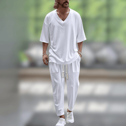 Uomo in abbigliamento casual bianco, con t-shirt e pantaloni larghi, cammina all'aperto. Stile estivo, moda maschile, look rilassato.
