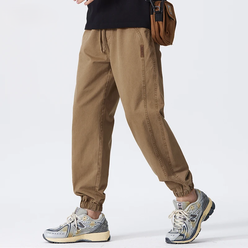 Pantaloni cargo uomo marroni, stile casual, con tasche laterali, abbinati a scarpe da ginnastica grigie e bianche. Moda streetwear maschile.