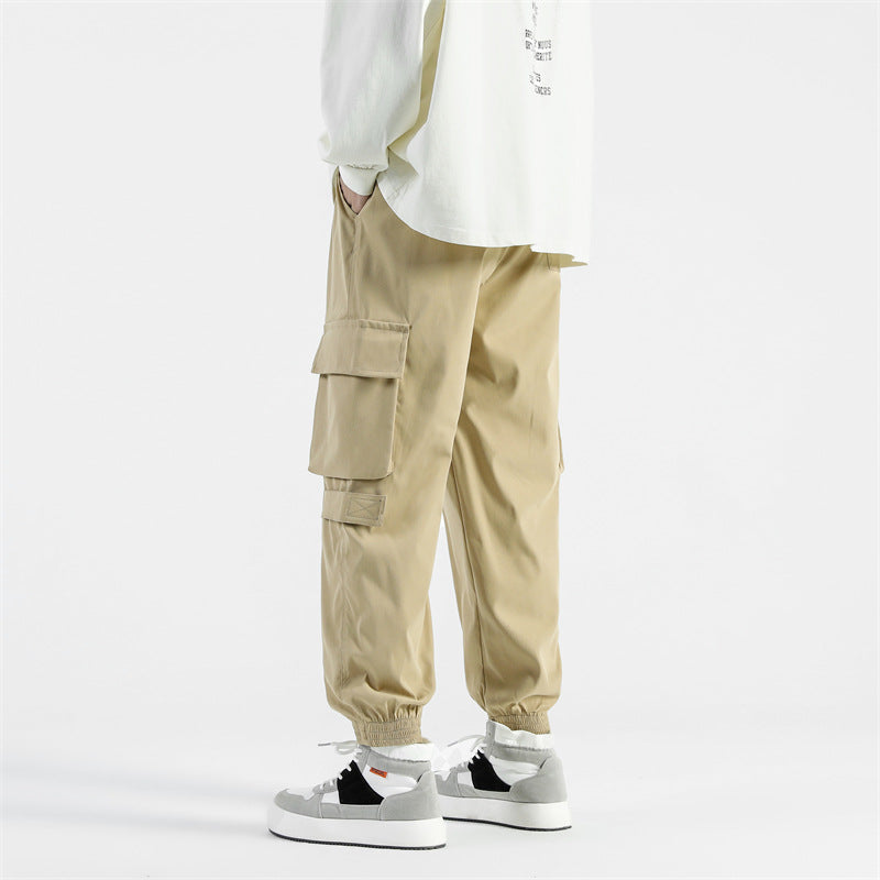 Pantaloni cargo beige da uomo, tasche laterali, stile casual, abbinati a scarpe da ginnastica bianche e nere, moda streetwear.