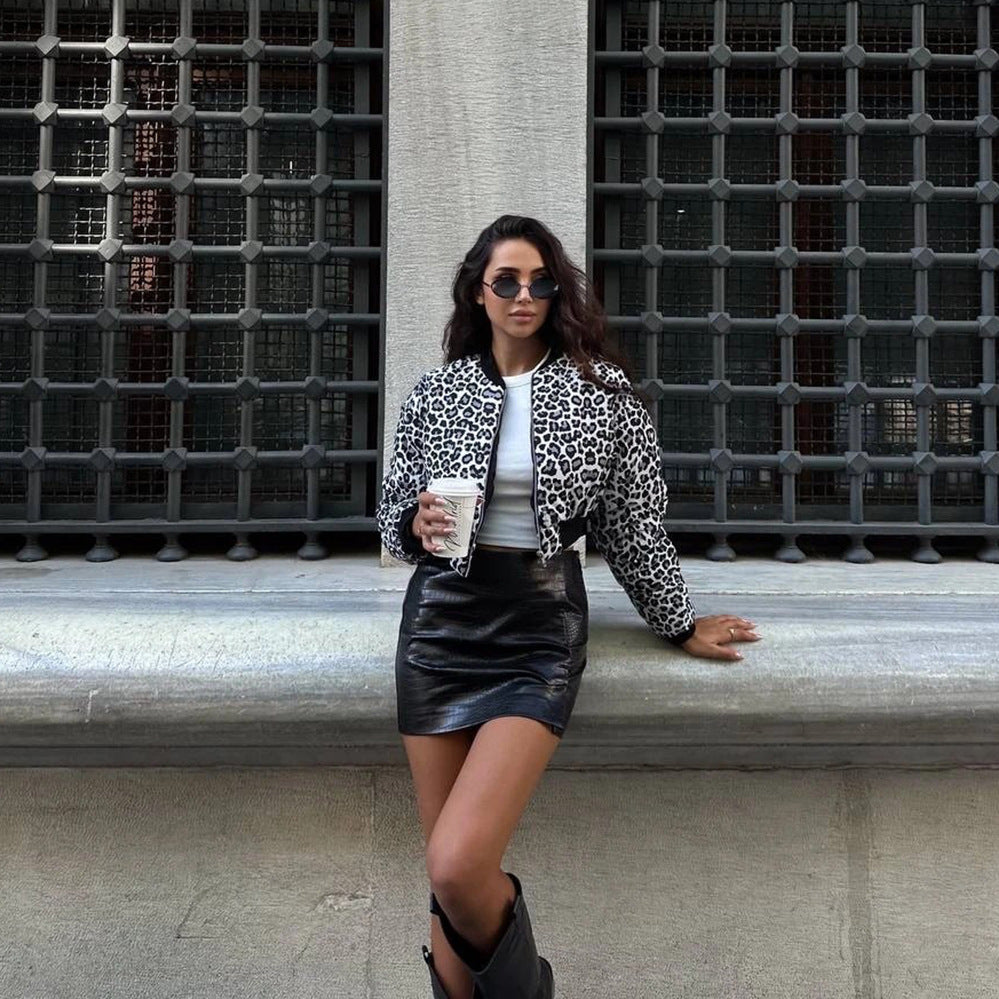 Donna con giacca leopardata, occhiali da sole e minigonna in pelle nera, tiene un caffè davanti a una grata metallica. Moda urbana, stile trendy.