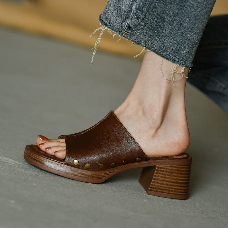 Sandalo marrone in pelle con tacco largo e borchie dorate, indossato con jeans sfrangiati. Scarpe estive eleganti, moda donna casual.