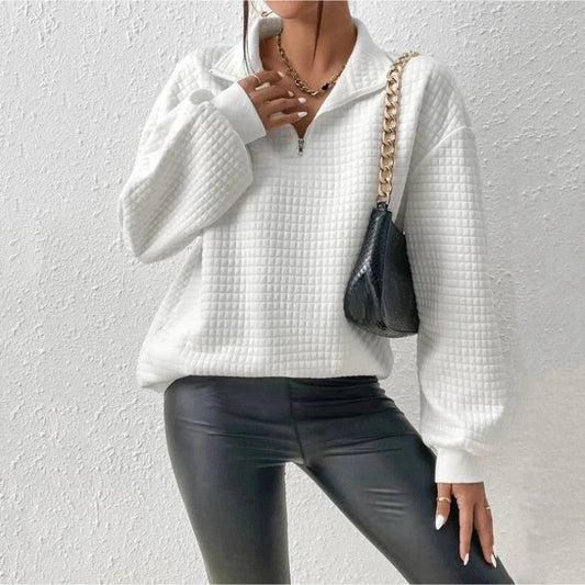 Donna con maglione bianco a quadri, pantaloni in pelle nera e borsa a tracolla con catena dorata. Moda autunnale, stile casual chic.