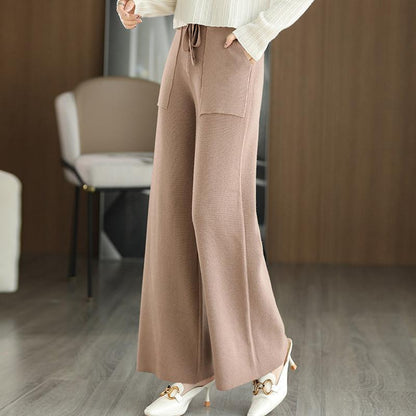Pantaloni larghi marroni in maglia, tasche frontali, indossati con maglione bianco e scarpe col tacco. Moda autunnale elegante e confortevole.