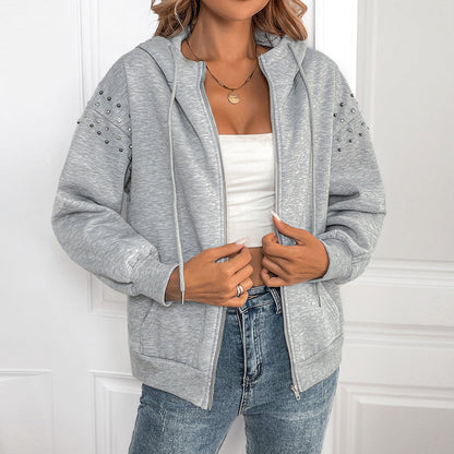 Donna con felpa grigia con cappuccio e borchie, indossa jeans e top bianco. Moda casual femminile, abbigliamento autunnale, stile urbano.