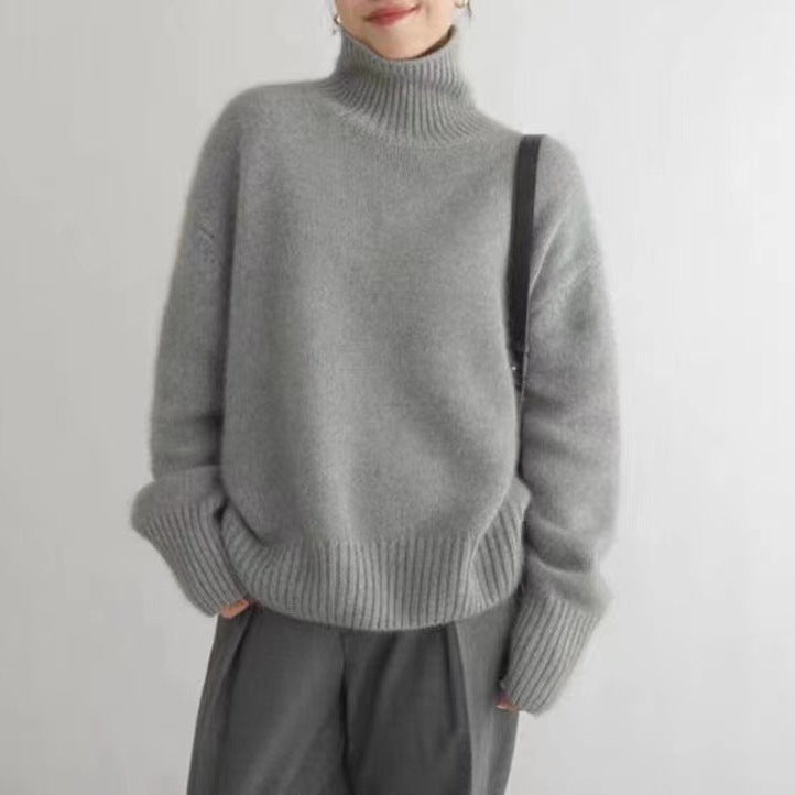 Maglione grigio a collo alto in lana, indossato da una persona con pantaloni grigi. Look invernale elegante e caldo, moda casual chic.