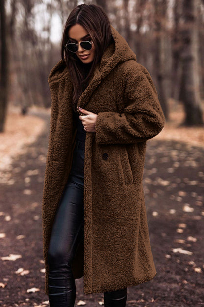 Donna con cappotto teddy marrone, occhiali da sole neri, pantaloni in pelle nera, in un parco autunnale. Moda autunno inverno, stile casual chic.
