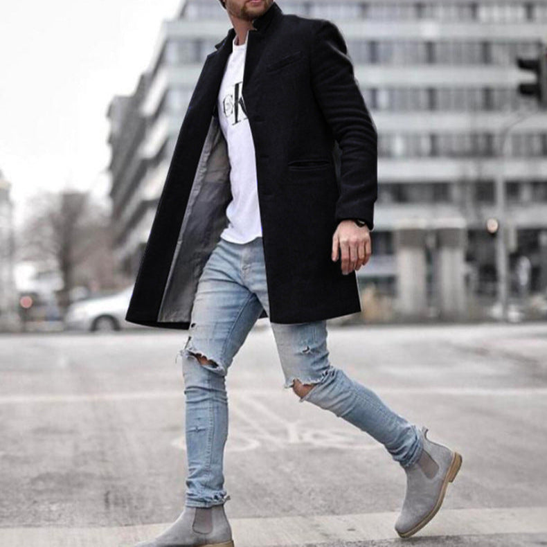 Uomo con cappotto nero elegante, jeans strappati e stivali grigi cammina in città. Moda maschile urbana, stile casual chic.