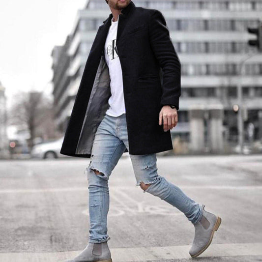 Uomo con cappotto nero elegante, jeans strappati e stivali grigi cammina in città. Moda maschile urbana, stile casual chic.