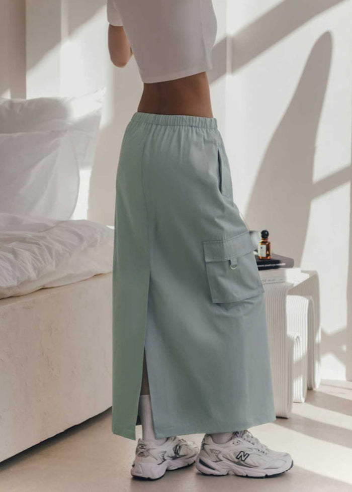 Donna in pantaloni cargo verde menta, top bianco, scarpe da ginnastica bianche, in una stanza luminosa con letto e comodino. Moda casual femminile.