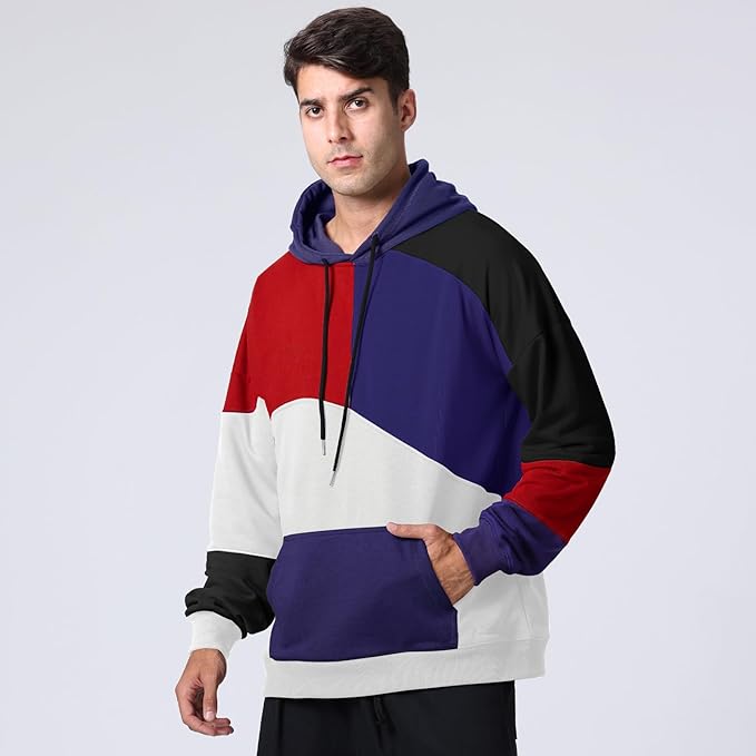 Uomo con felpa multicolore a blocchi rossi, blu, bianchi e neri, cappuccio e tasca frontale. Moda casual, abbigliamento streetwear.