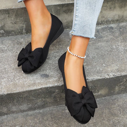 Scarpe ballerine nere con fiocco grande, indossate su gradini di cemento. Moda donna, calzature eleganti, jeans chiari, cavigliera perla.
