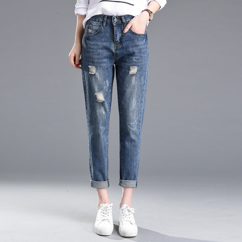 Jeans strappati da donna, stile casual, colore blu, con risvolti alla caviglia. Indossati con scarpe bianche su sfondo grigio.