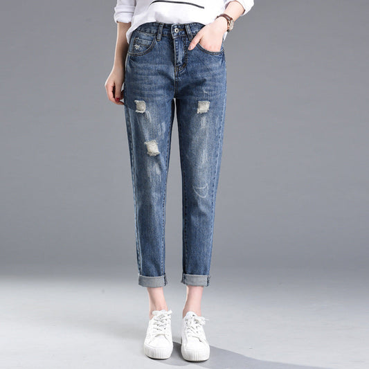 Jeans strappati da donna, stile casual, colore blu, con risvolti alla caviglia. Indossati con scarpe bianche su sfondo grigio.