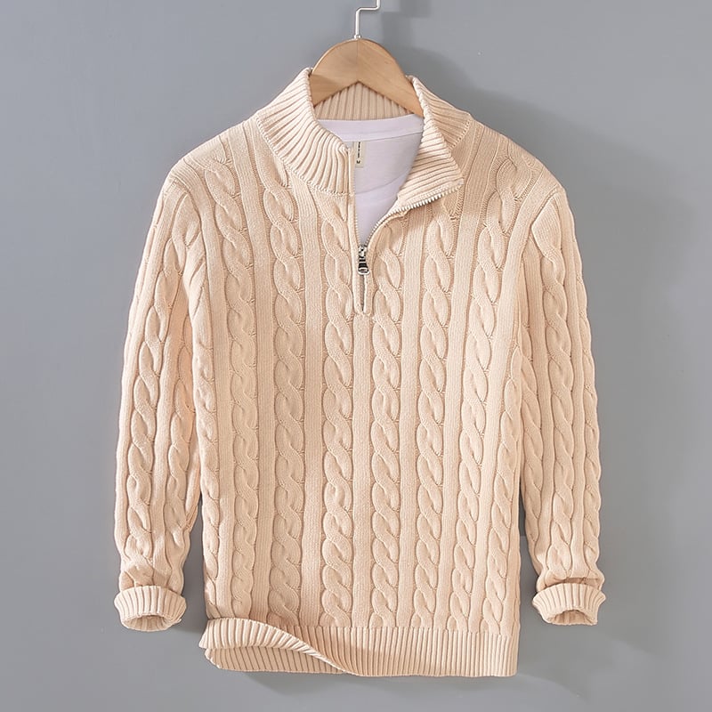 Maglione beige a trecce con zip, appeso su gruccia di legno, sfondo grigio. Moda autunnale, abbigliamento casual, stile elegante.
