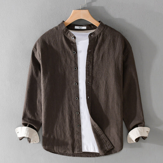 Camicia casual marrone in lino con colletto alla coreana, bottoni frontali, maniche lunghe e polsini bianchi, appesa su gruccia di legno.