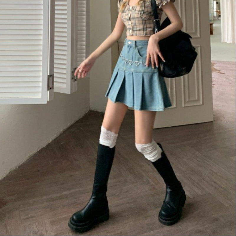 Giovane donna con gonna di jeans a pieghe, top a quadri, stivali neri alti e calze bianche, in posa in un interno moderno. Moda casual chic.