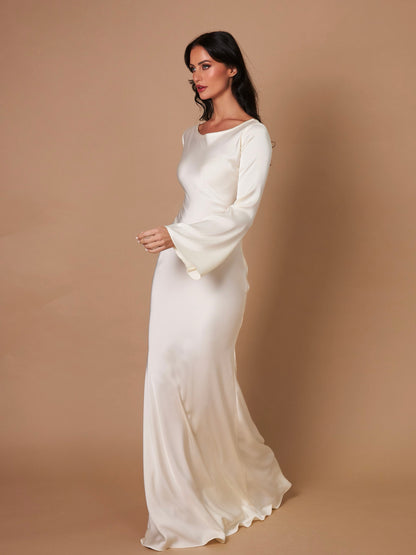 Donna in abito da sera bianco avorio, maniche lunghe, su sfondo beige. Moda elegante, abbigliamento formale, tendenza abiti da cerimonia.