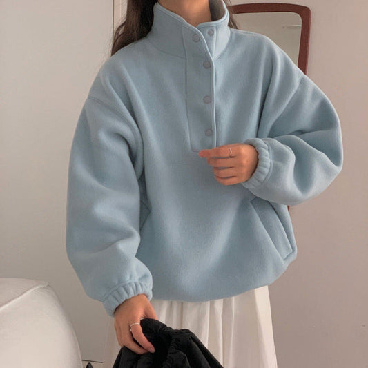 Donna con maglione oversize azzurro, collo alto e bottoni, in una stanza minimalista. Moda autunno inverno, abbigliamento casual elegante.