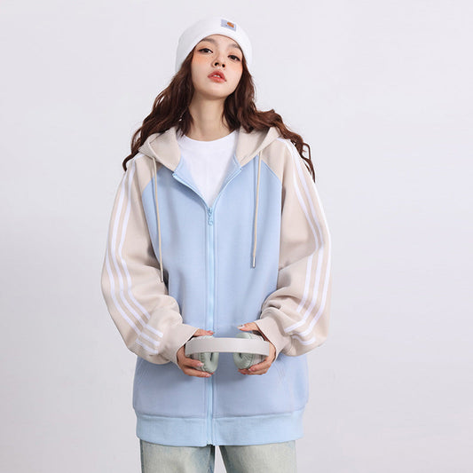 Giovane donna con felpa con cappuccio azzurra e beige, cappello bianco, tiene cuffie. Moda casual, abbigliamento streetwear, stile urbano.